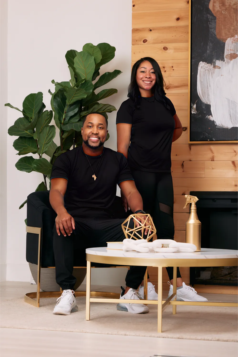Jerod seated and Fancy standing beside him in a living room with a fiddle-leaf fig and a gold coffee table